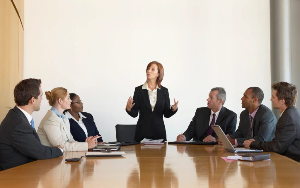 A woman standing in front of several people at a table.